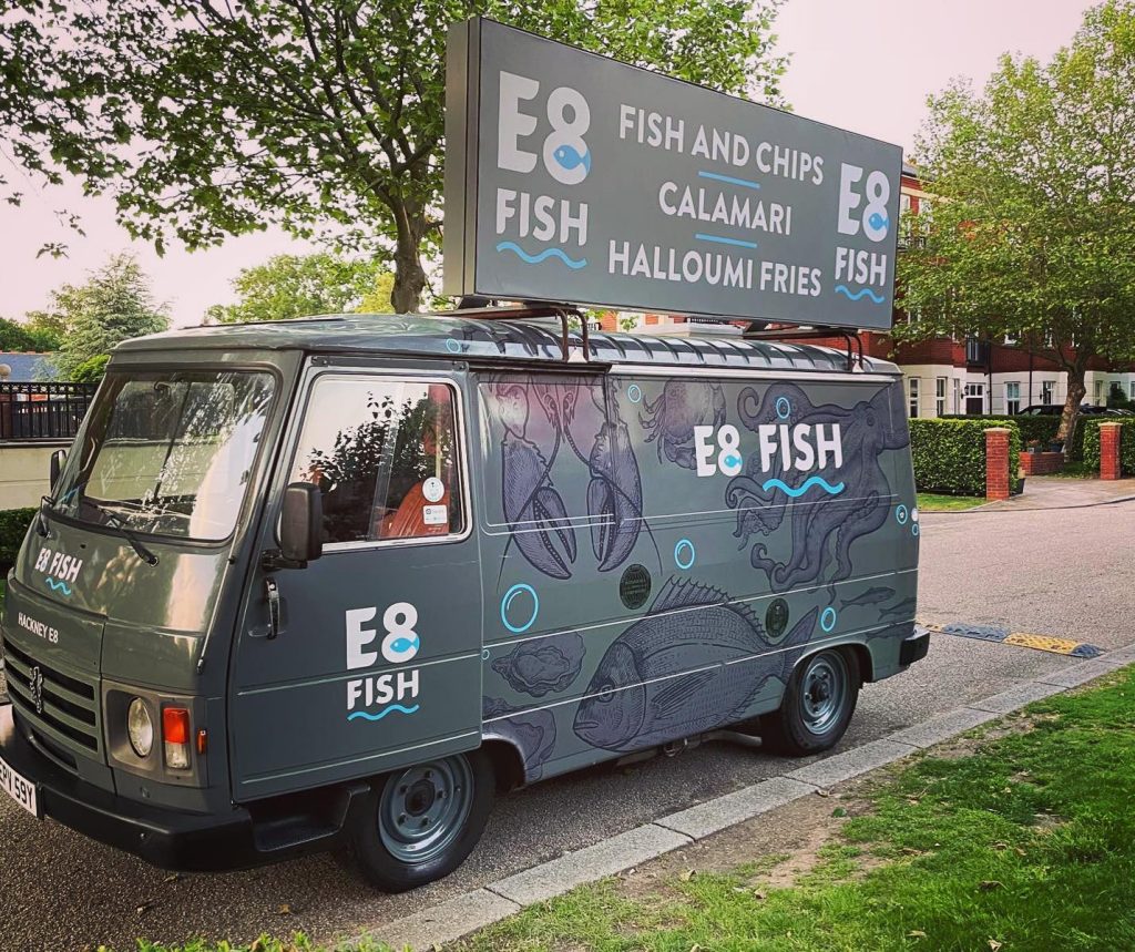 A van that is grey with lobsters on it and has the logo E8 FISH. It sells fish and chips from it.