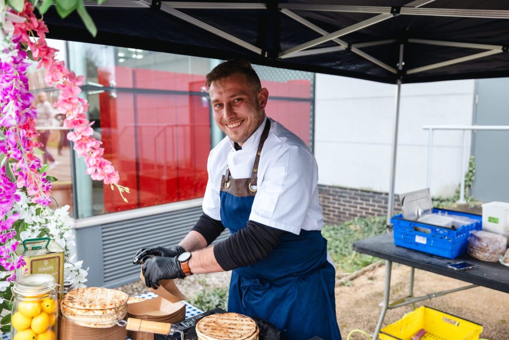 A chef in a white outfit and blue apron preparing greek gyros.