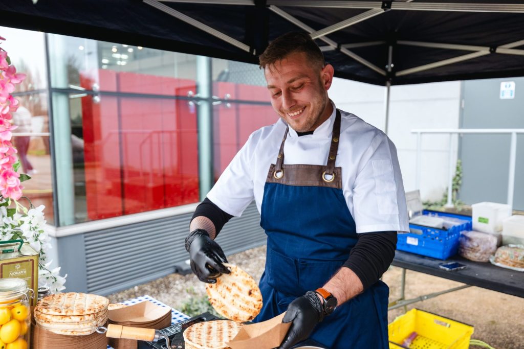 A chef in a white outfit and blue apron preparing greek gyros.