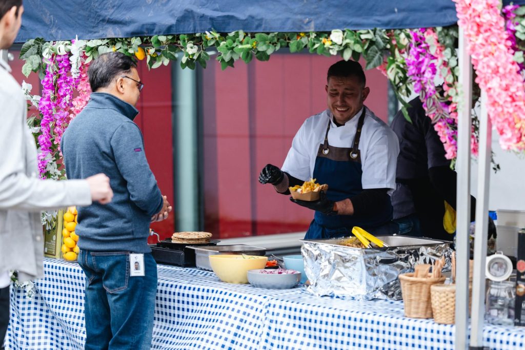 A chef in a white outfit and blue apron preparing greek gyros.